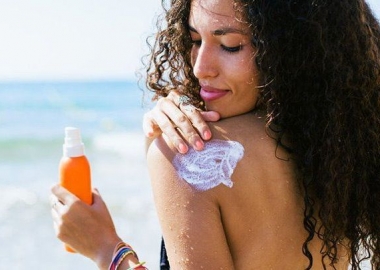 A Black woman at the beach applying sunscreen to her left shoulder. (Photo: BonninStudio/Stocksy)