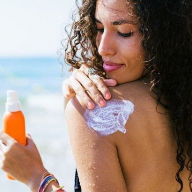 A Black woman at the beach applying sunscreen to her left shoulder. (Photo: BonninStudio/Stocksy)