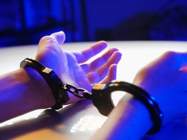 Man's arms in handcuffs resting on a table. (Photo: Kindel Media/Pexels)