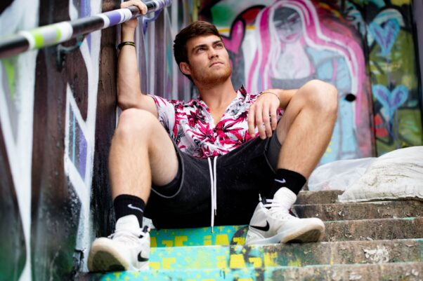 A man sitting on steps outside weaing a floral print white and pink shirt, black shorts, black Nike socks and white and black Nike high-top sneakers. (Photo: Brian Lundquist/Unsplash)