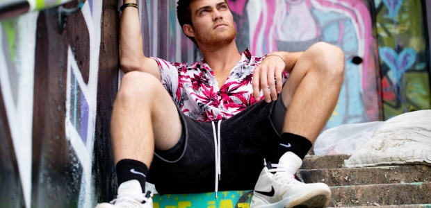A man sitting on steps outside weaing a floral print white and pink shirt, black shorts, black Nike socks and white and black Nike high-top sneakers. (Photo: Brian Lundquist/Unsplash)