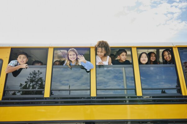 Medium wide shot of smiling middle school kids looking out open windows of school bus. (Photo: Penn State Health)