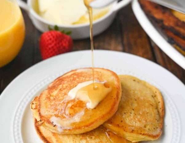 Hoe cakes on a white plate with maple syrup being poured on them from above.