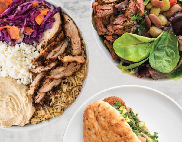 Two different steak and chicken bowls and a pita sandwich from Roti on plates sitting on a white table top. (Photo: Roti)