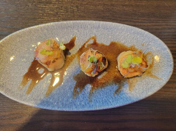 Three pan-seared scallops served on top of a brown butter sauce on a white plate. (Photo: Mark Heckathorn/DC on Heels)