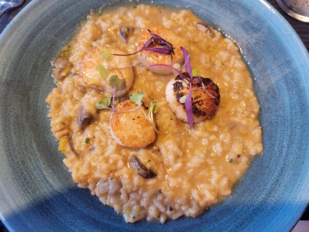 Four pan-seared scallops on top of butternut squash risotto in a shallow light blue bowl. (Photo: Mark Heckathorn/DC on Heels)