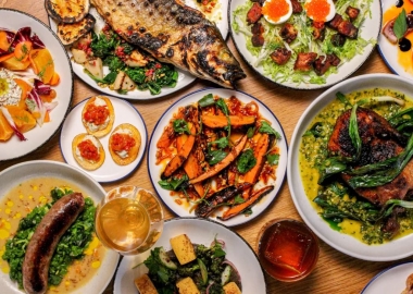 An assortment of dishes including a whole branzino on white plates atop a wooden table. a.kitchen+bar specializes in seasonal American ingredients and natural wines. (Photo: a.kitchen+bar)