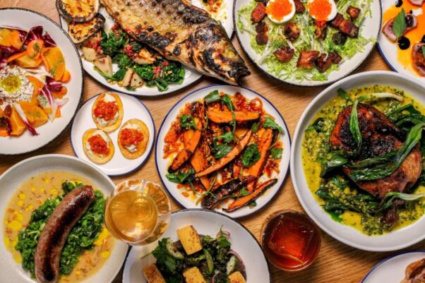 An assortment of dishes including a whole branzino on white plates atop a wooden table. a.kitchen+bar specializes in seasonal American ingredients and natural wines. (Photo: a.kitchen+bar)