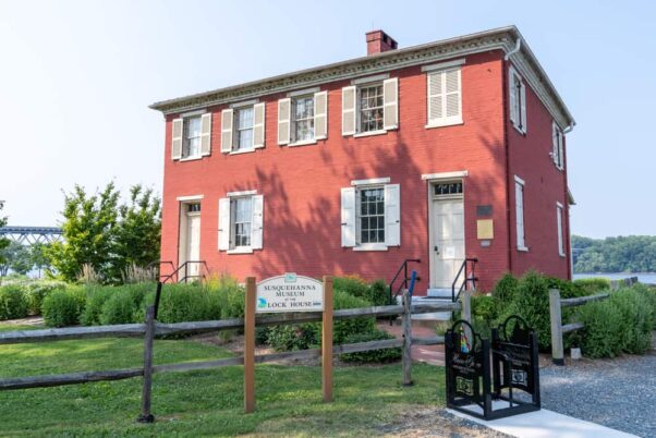 Outside of the red brick Lock House Museum with white shutters behind a split rail fence. (Photo: Rosemarie Mosteller/Shutterstock)