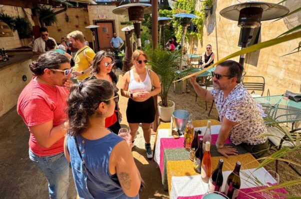 Three women and a man stand in front of a table holding several wine bottles talking with a vineyard representative. (Photo: Lulu's Winegarden)