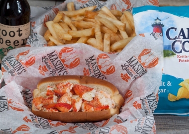 A lobster roll in a basked with red and white paper surrounded by French fries, a bag of chips and a bottle of soda. (Photo: Mason's Famous Lobster Rolls/Facebook)