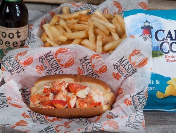 A lobster roll in a basked with red and white paper surrounded by French fries, a bag of chips and a bottle of soda. (Photo: Mason's Famous Lobster Rolls/Facebook)