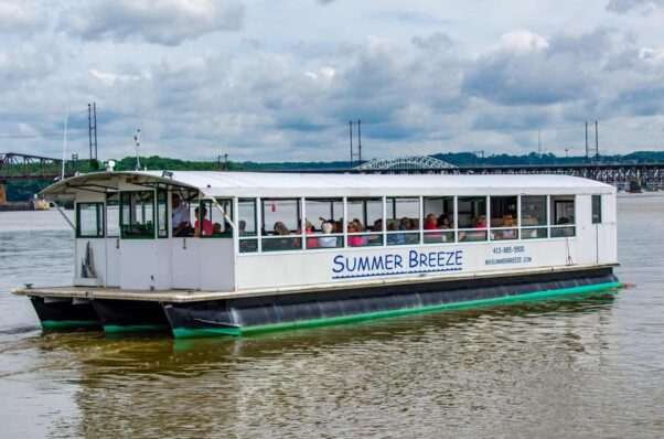 The white M/V Summer Breeze with blue writing and a room sails on the Susquehanna River with passengers onboard and a bridge in the background. (Photo: M/V Summer Breeze)