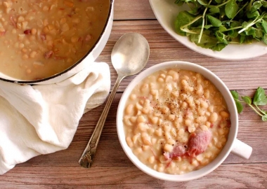 A white bowl filled with Senate Bean Soup on a table with the pot of soup, a salad and a spoon. (Photo: Contributed)