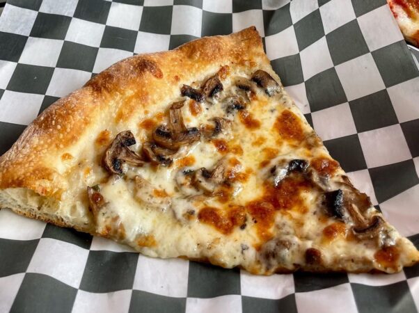 A slice of Slice & Pie's Truffle pie with parmesan cream, mozzarella, mushroom, garlic, truffle oil and parsley sitting on a piece of black and white paper. (Photo: Slice & Pie/Facebook)