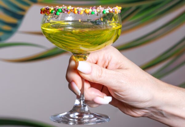 A woman's hand holding a greenish-yellow martini with Nerds around the rim. (Photo: Jonni Scott Photography)