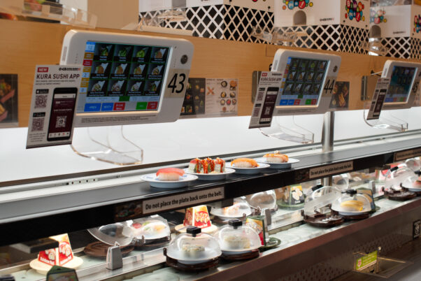 Four plates of uncovered sushi arrives directly to a table on the top conveyor belt while covered plates circulate the dining room on the lower belt. A touch screen is mounted above the two belts for diners to order. (Photo: Emily J. Davis/Kura Sushi)
