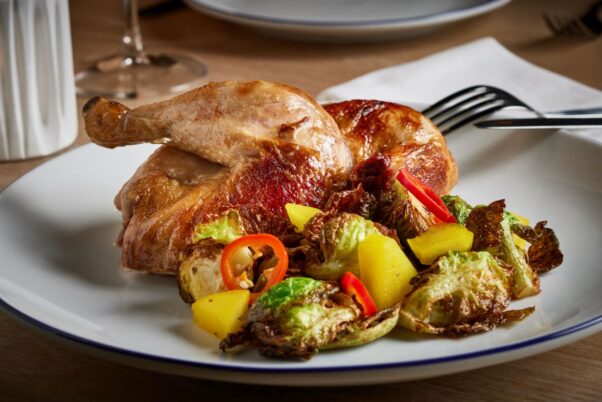 Rosedale's rotisserie, organic chicken with a Brussels sprouts salad on a white plate with a fork & knife beside it. (Photo: Greg Powers)