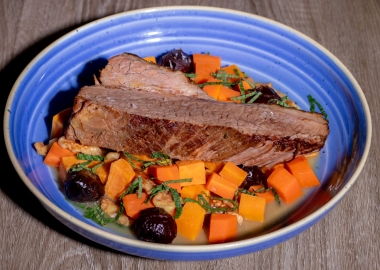 Braised brisket with carrots, sweet potato and walnut and date tzimmes in a blue bowl sitting on a wooden table. (Photo: Sababa)