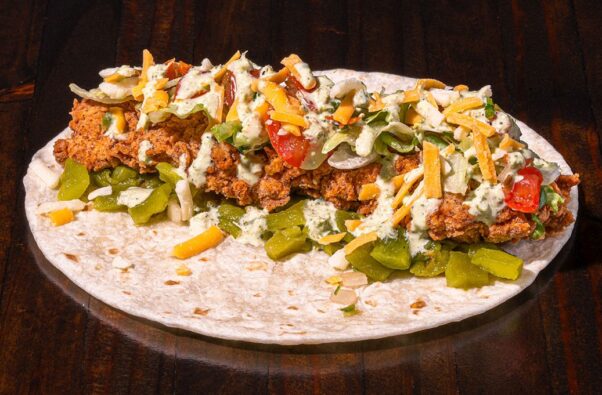 Torchy's Trailer Park taco with fried chicken, green chiles, lettuce, pico de gallo, mixed cheese and poblano sauce on a flour tortilla sitting on a wood table. (Photo: Torchy's Tacos)