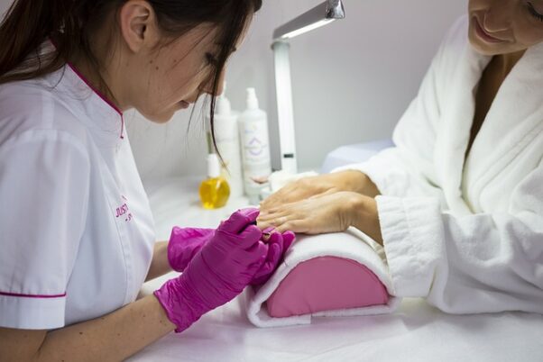 A woman in a white robe getting a manicure from a woman wearing pink gloves. (Photo: Spabielenda/Pixabay)