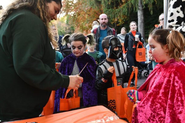 Children at the Boo at the Zoo family-friendly Halloween event dressed in costumes get candy from a female volunteer. (Photo; National Zoo)