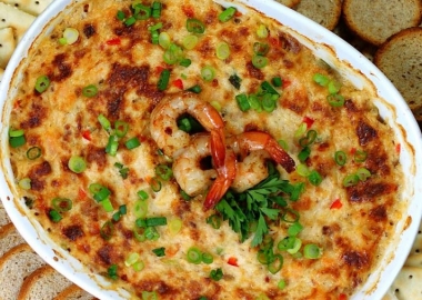 Hot, browned crab and shrimp dip with spinach in a white, ceramic baking dish with a few whole shrimps on top and bread and crackers around the dish. (Photo: Contributed)