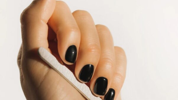 A woman with dark red nails files them with an emery board. (Photo: Getty Images)