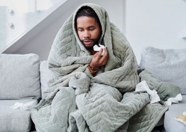 A young Black man with the flu sitting on the couch at home. (Photo: Getty Images)