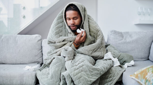 A young Black man with the flu sitting on the couch at home. (Photo: Getty Images)