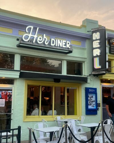 The exterior of Her Diner. The building is painted light green with a sign above windows & an awning with metal tables & chairs in front. (Photo: Michael Glasser/Instagram)