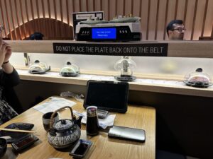 Sushi moves past a table set with earthenware plates & a tea pot on a conveyor belt at Kanji Sushi & Bar. (Photo: Jiaxin I/Yelp)
