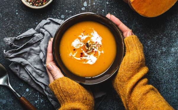 A woman's hands hold a black bowl full of pumpkin soup topped with sour cream and pumpkin seeds. (Photo: Contributed)