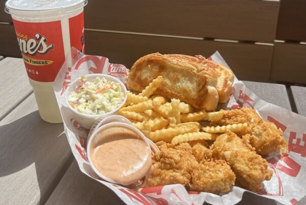 A Raising Cane's four-piece chicken strip meal with Texas toast, coleslaw and Cane's sauce beside a large drink sitting on a picnic table. (Photo: Raising Cane's/Facebook)