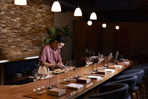 Chef Johnny Li, standing behind the counter, prepares sushi at Raw. The bar is set for diners with blocks of wood to serve the sushi on, wine and water glasses, and chopsticks. (Photo; Deb Lindsey)