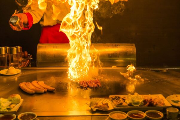 Four sausages cook on a hibachi while flames shoot up after a chef squirts oil on the grill. (Photo: Sake Japanese Steak House/Facebook) 