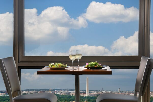 A table set with 2 glasses of white wine and two salads overlooking Washington, DC from the Skydome restaurant. (Photo: Skydome/Instagram)