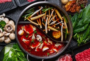 A divided hot pot with different broths and mushrooms in each side surrounded by raw meats and vegetables. (Photo: T Pot Hot Pot & Korean BBQ) 