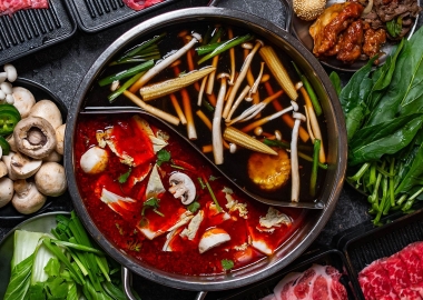 A divided hot pot with different broths and mushrooms in each side surrounded by raw meats and vegetables. (Photo: T Pot Hot Pot & Korean BBQ)