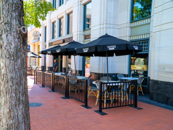 The exterior of Taffer's Tavern in Chinatown with a fenced outdoor seating area with tables, chairs and open umbrellas. (Photo: Taffer's Tavern/Facebook)