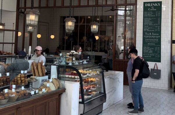 Two customers stand at the counter in Tatte Bethesda looking at good in a display case with 2 employees are behind the counter. (Photo: Tatte)