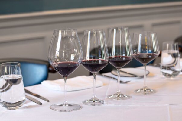 Four wine glasses filled with red wine sit in a row on a table with a white tablecloth set with silverware and a napkin. (Photo: Jonnis Scott Photography)