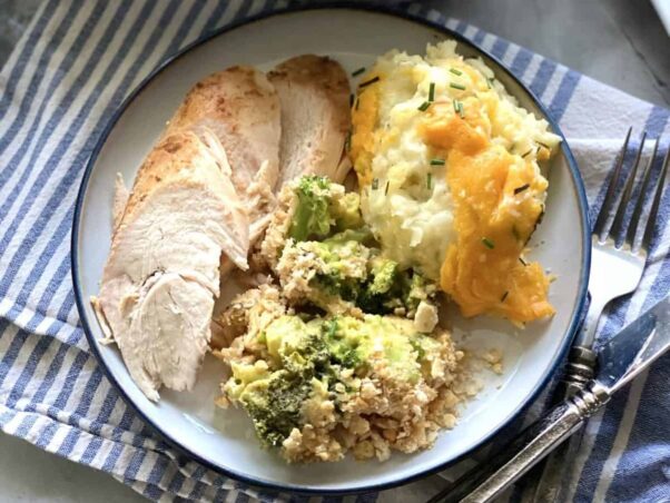 Broccoli and cheese casserole with Ritz crackers on a white plate with slices of turkey breast and cheesy scalloped potatoes. (Photo: Katie Jasiewicz)