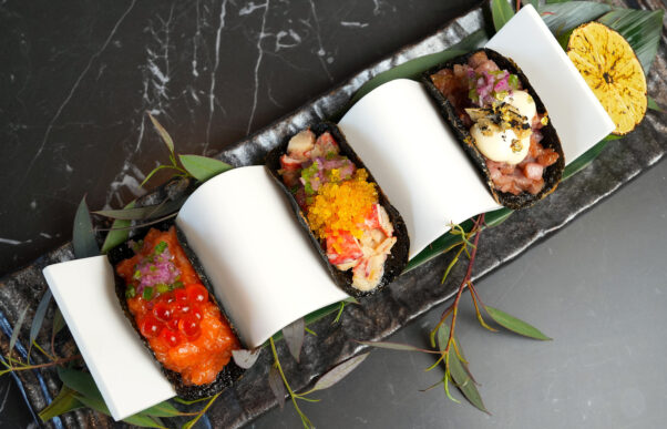 Three "tacos" made with nori shells and topped with gold leaf sit in a taco holder. (Photo: eJin)