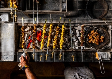 Skewers of meat cook on a charcoal grill at Yellow while other meat cooks in a pan. (Photo: Rey Lopez)