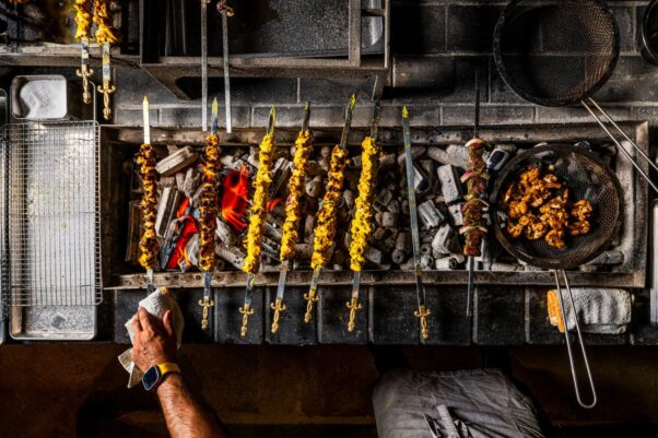 overhead shot of skewers of meat cooking on a charcoal grill at Yellow while other meat cooks in a pan. (Photo: Rey Lopez)