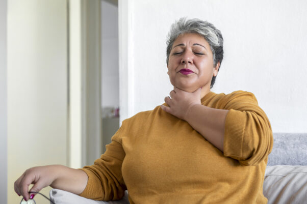 A woman suffering from acid reflux or heartburn holds her throat and closes her eyes. (Photo: Getty Images)