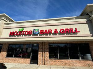 Exterior of Mojitos Bar & Grill in red brick and beige stucco building with red & green letters above door & windows. (Photo: Screenshot)