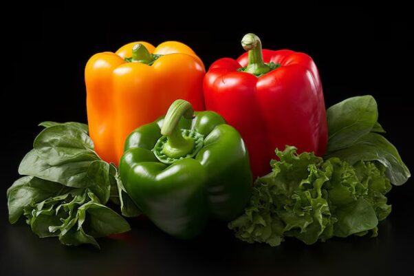 An orange, green and red bell pepper surrounded by leafy greens. (Photo: Freepik)