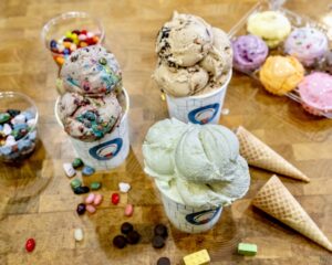 Three cups filled with scoops of ice cream surrounded by sugar cones, jelly beans M&Ms and other toppings. (Photo: Sarah's Homemade Ice Cream)